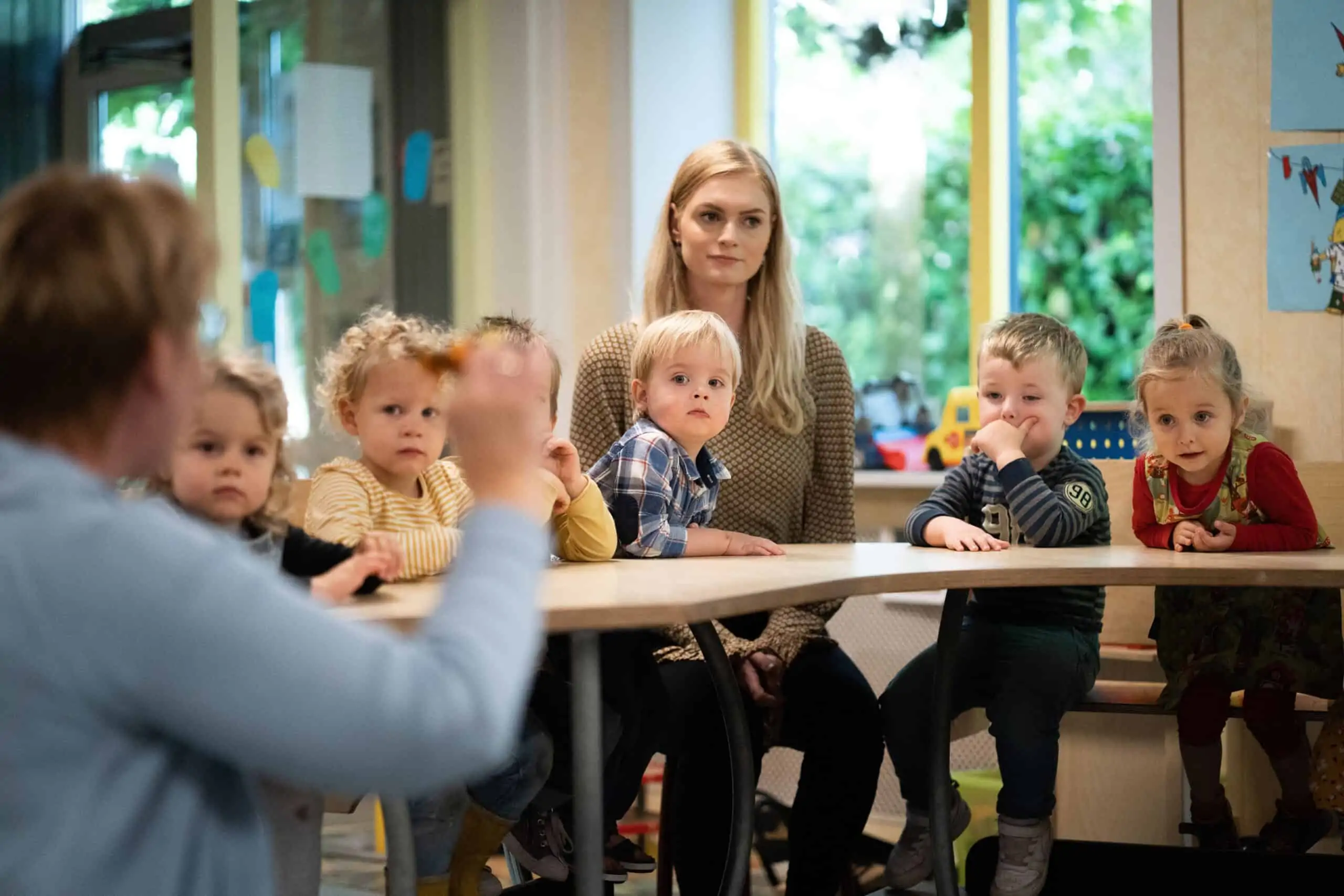 Kinderen zitten samen met twee pedagogisch medewerkers aan tafel bij Poespas